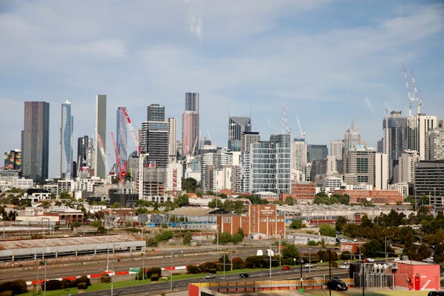 View of Melbourne's skyline featuring tall skyscrapers and construction cranes under a clear sky. Bhullar Graphic