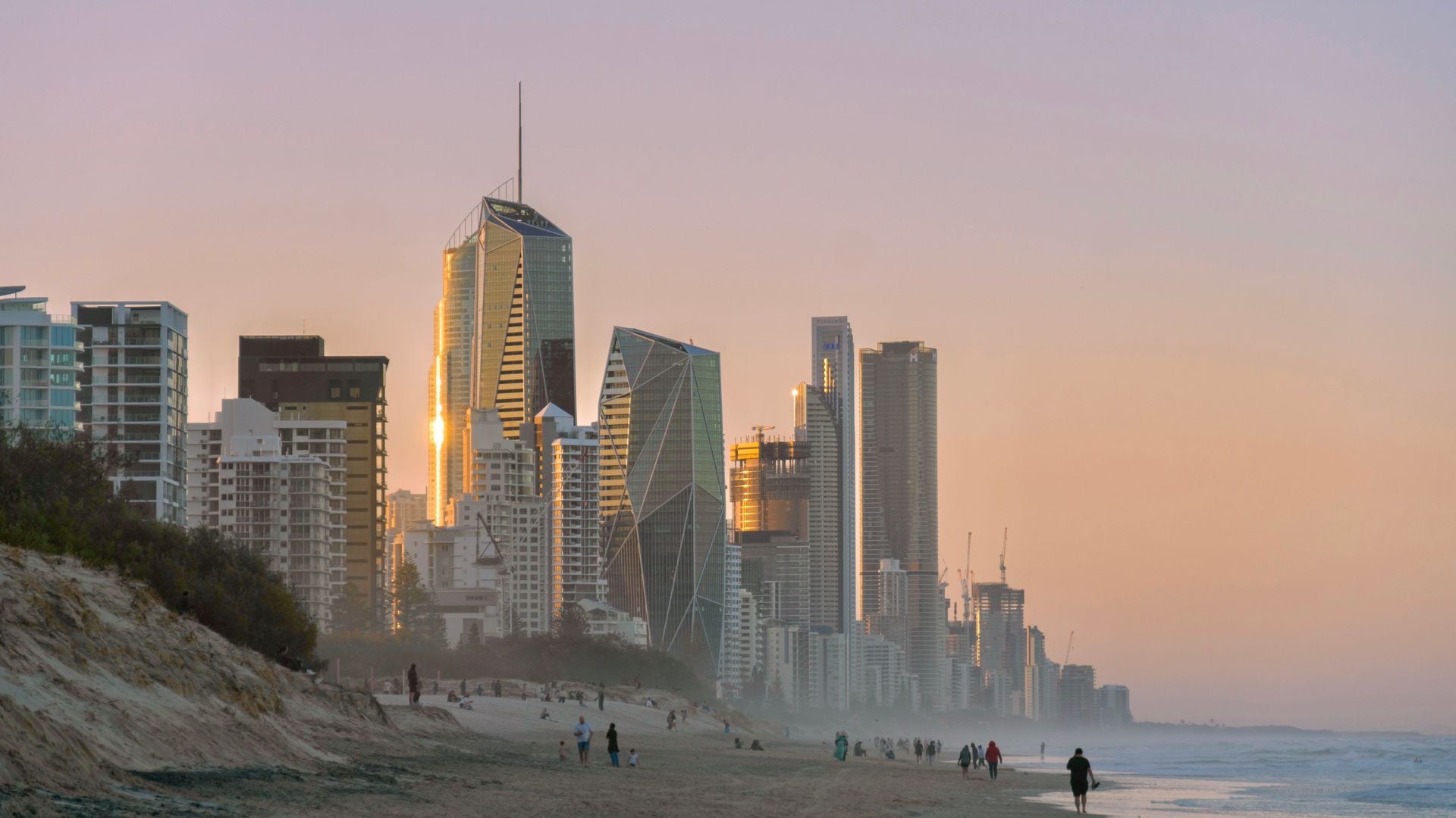 Beautiful sunset view of Surfers Paradise skyline, with beachfront and people walking on the sand.
